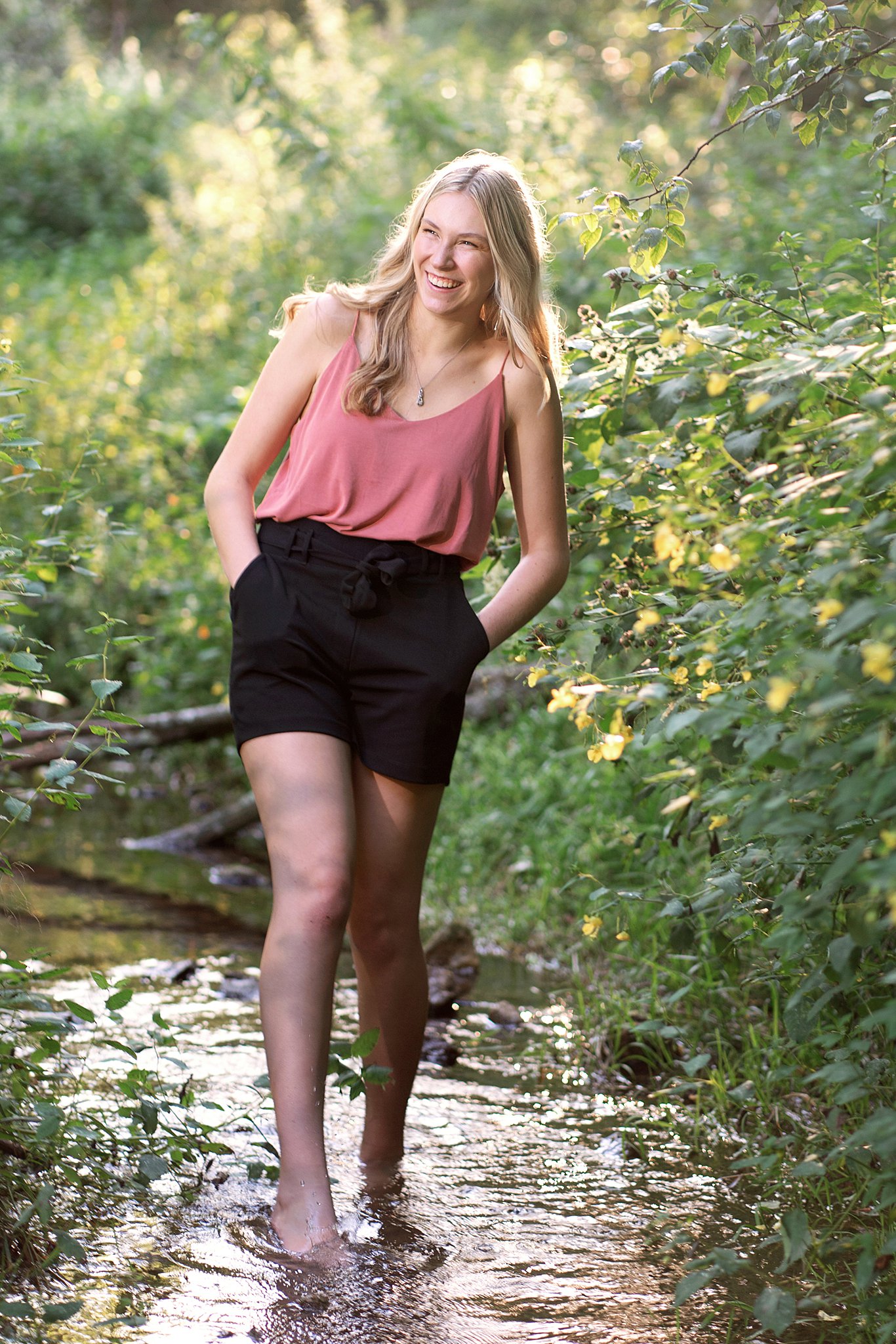 high school senior in pink top and black shorts from clothing boutiques in Rochester MN playing in the stream
