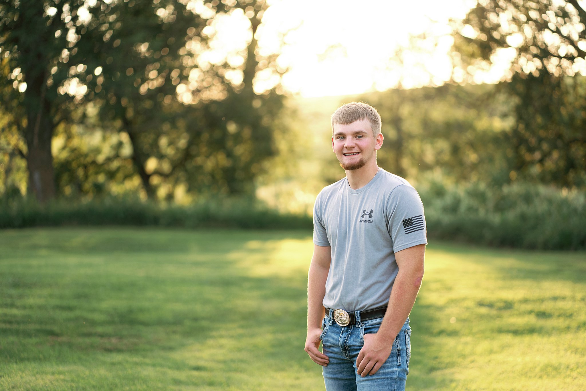 senior guy in grey tshirt and blue jeans standing in a field in Minnesota