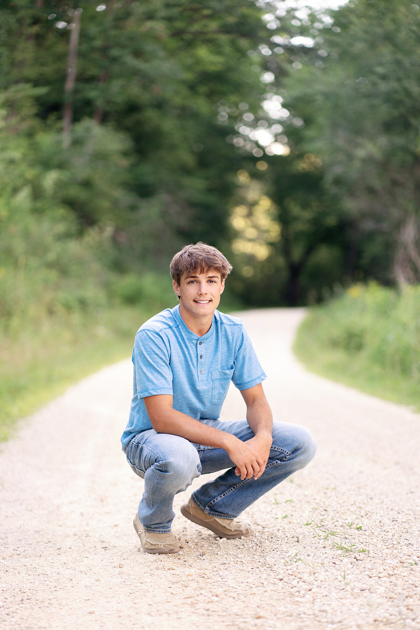 senior boy with blue shirt and jeans crouching in the road