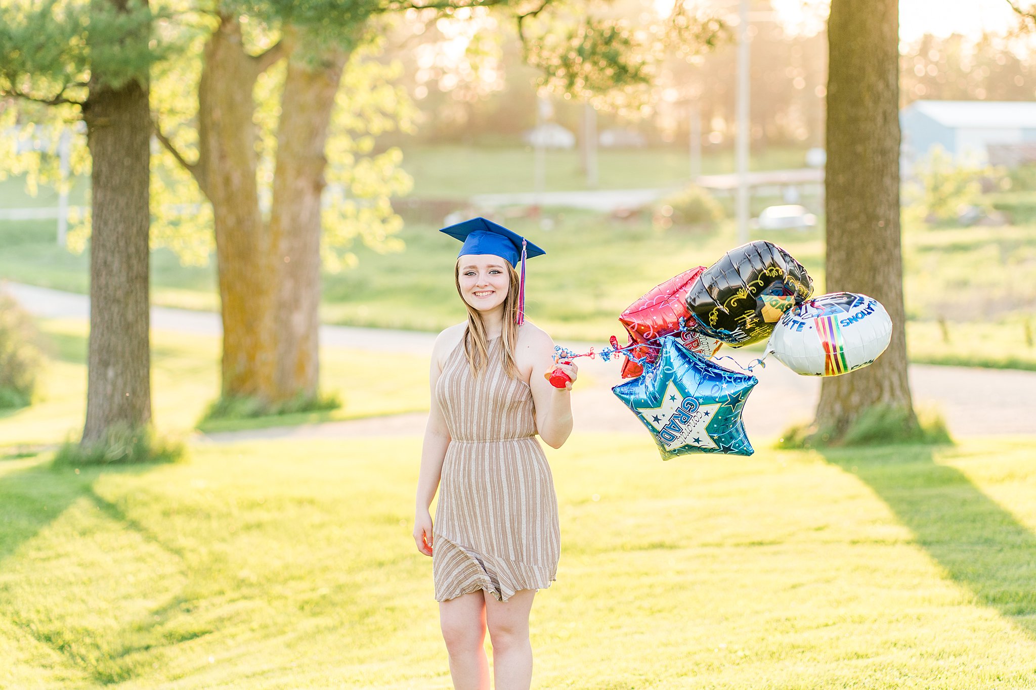 High school graduate stands in a park holding celebratory balloons