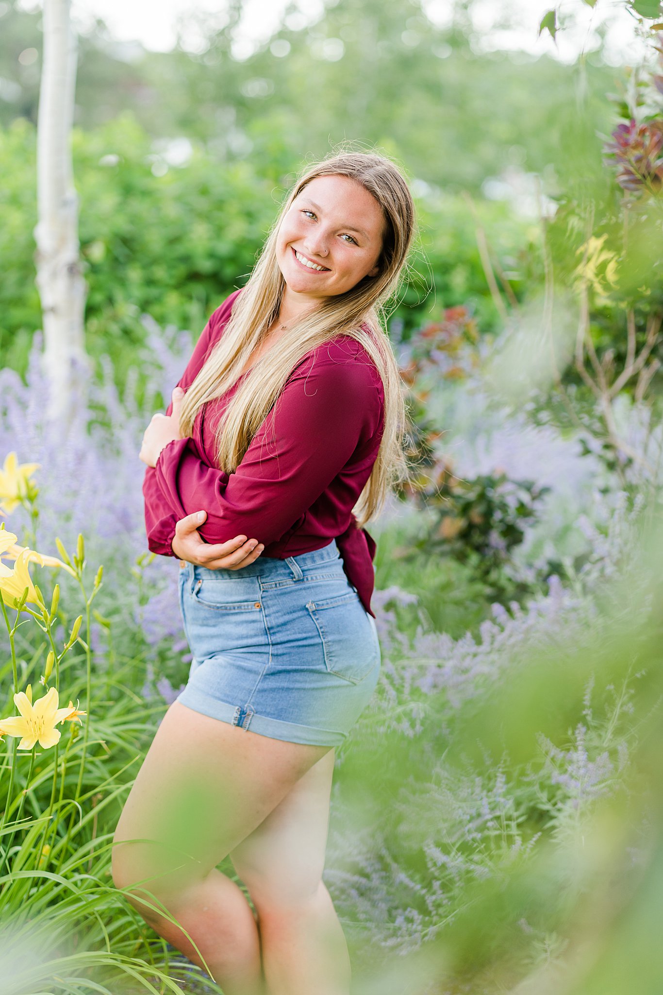 High school senior stands with arms crossed in a flower garden