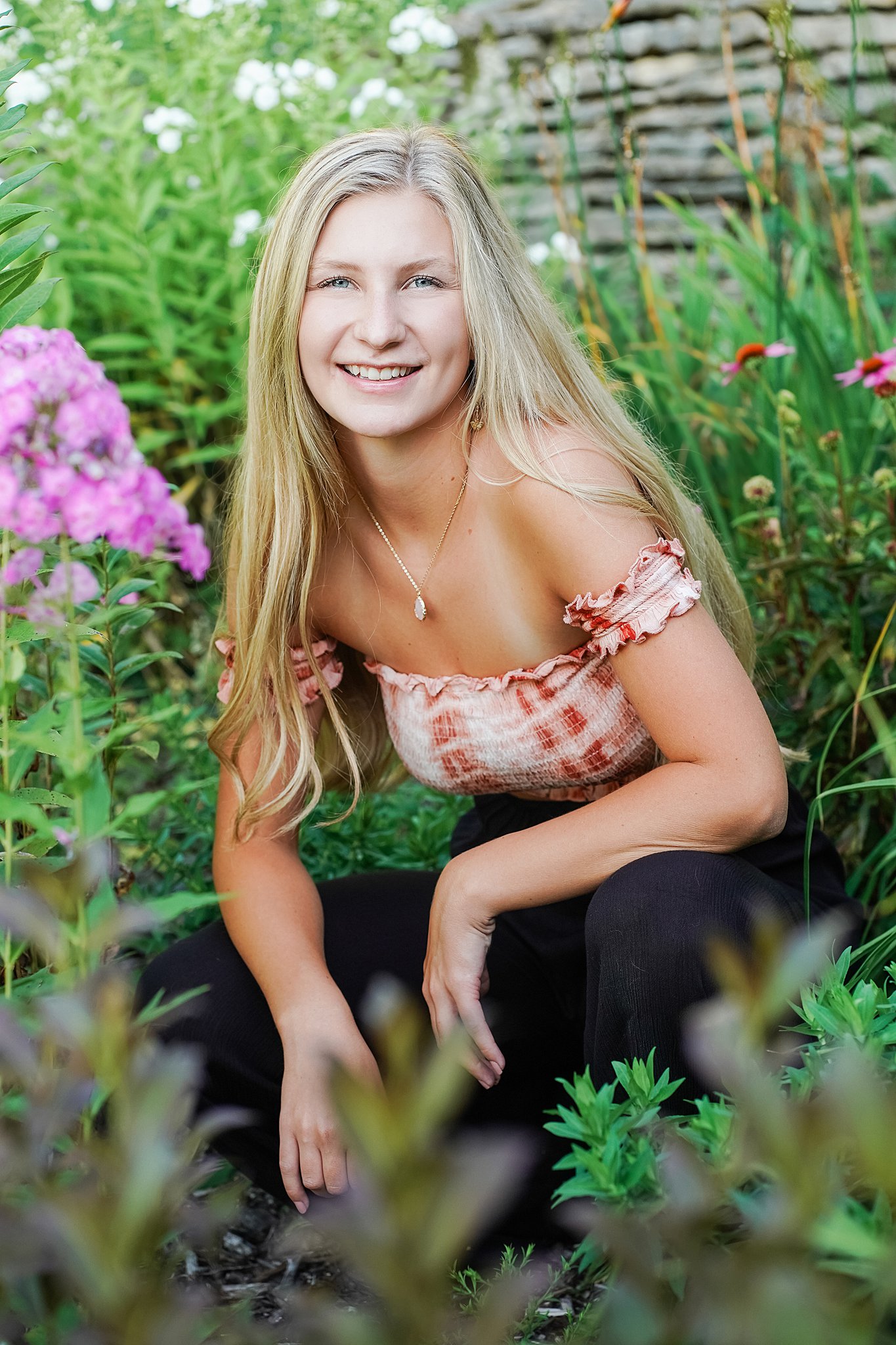 High school senior crouches in a colorful flower garden mabel canton high school