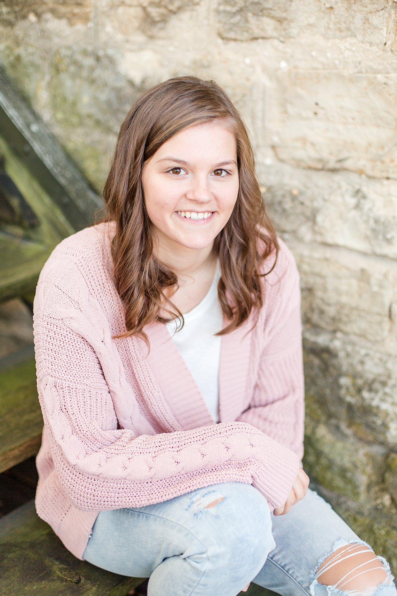 girl sits in a rustic stonework stairwell in a pink sweater mayo senior high school