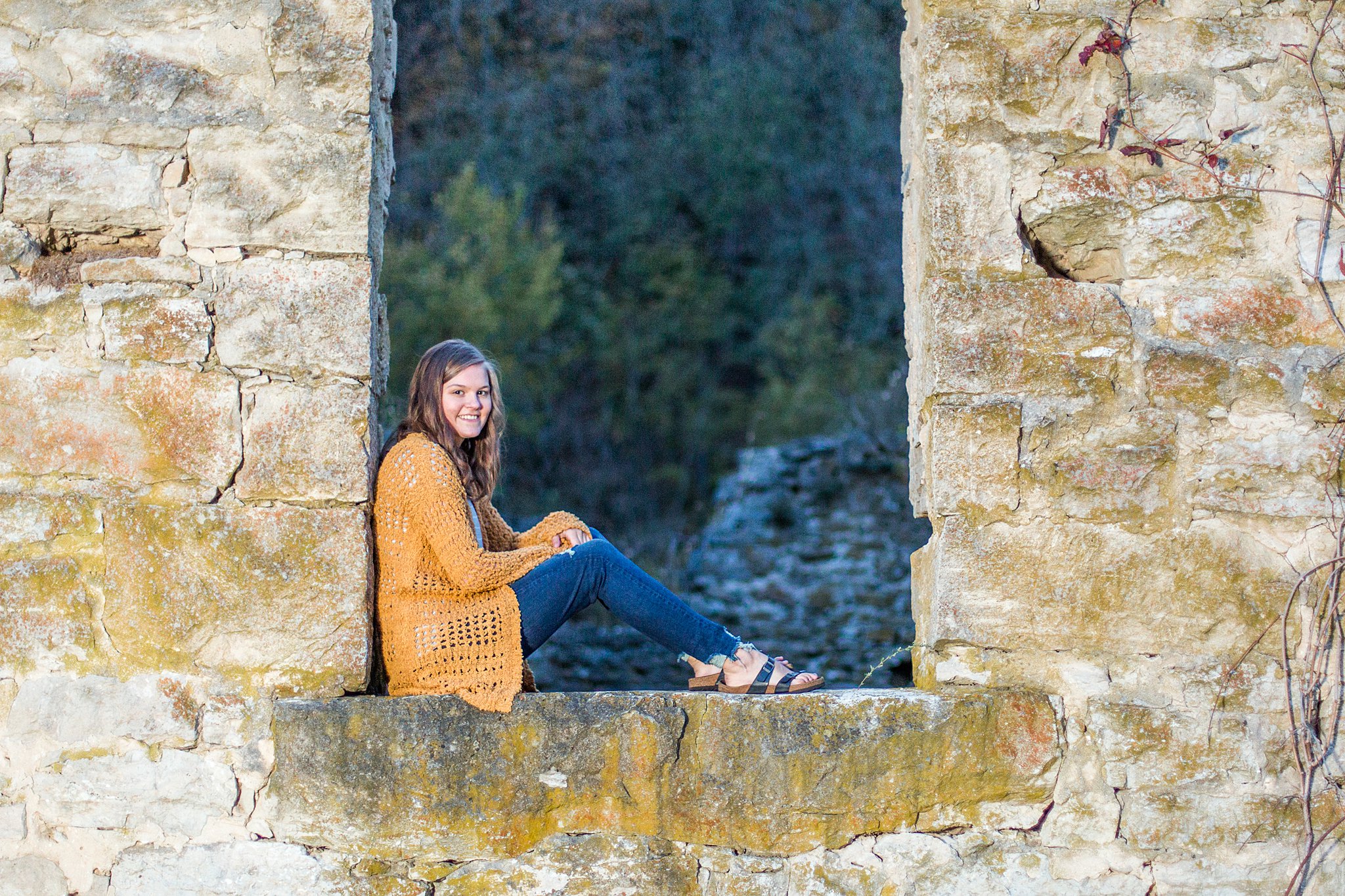 teenage girl sits in an opening of old stonework wearing brown knit sweater and jeans mayo senior high school