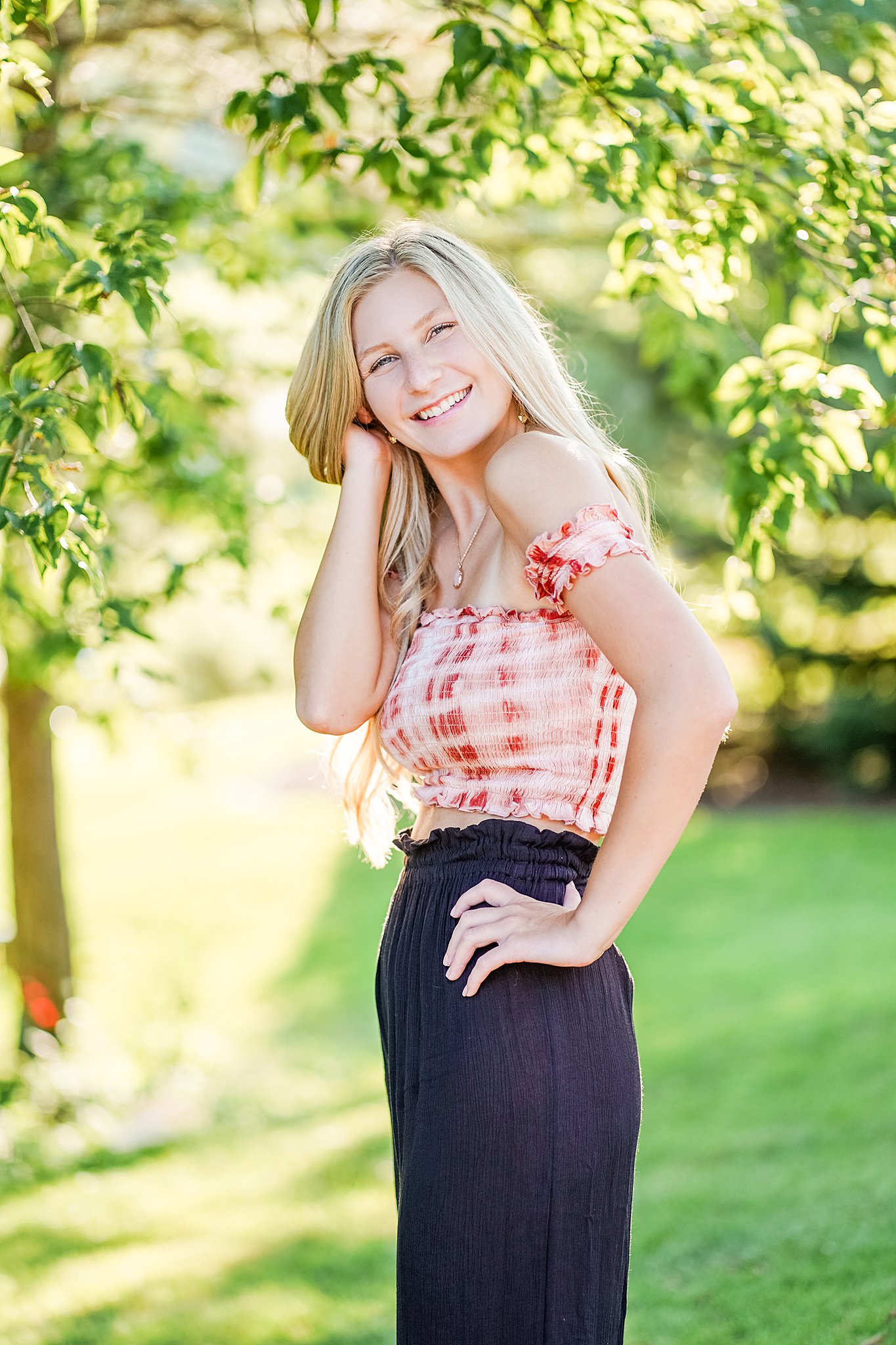 High school senior stand in a green yard with hand on her hip
