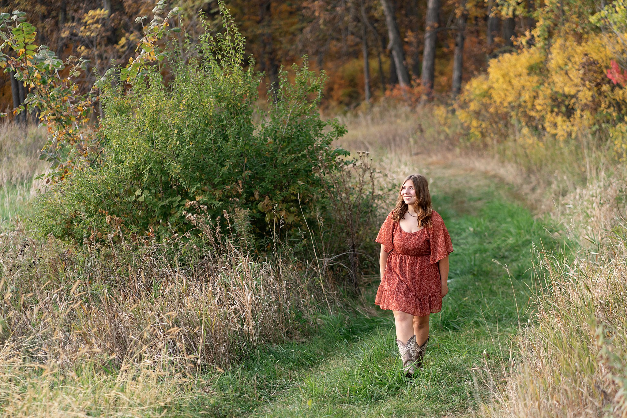 Teenage girl walks down an overgrown patch in boots andd a red dress stewartville high school